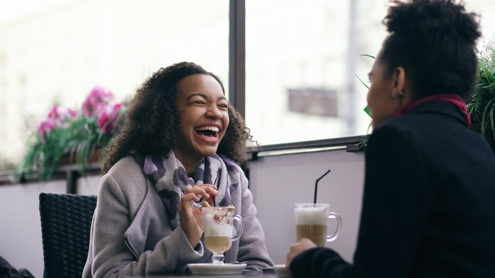 Two friends laughing over coffee at a street café